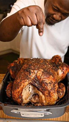 a man pointing at a roasted chicken in a pan