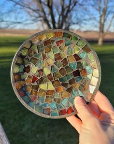 a hand holding up a glass plate that is made out of small pieces of mosaic tile