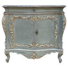 an ornately painted cabinet with gold trimmings on the doors and drawers, against a white background