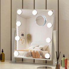 a mirror that has lights on it in front of a table with a vase and other items