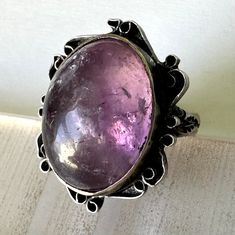 "a lovely older Mexican ring, likely from the thirties or forties.  the stone is an interesting amethyst with a high dome, the face has a wonderful curly edge, and the band has fabulous flower and leaf patterns.  the bezel has some kinks, not perfectly smooth, and the stone has the slightest wiggle.  marked 925 and in good vintage condition. size:  between 7 and 7.25 height of face:  1\" height off finger:  5/16\" width of inner band:  1/8\"" Antique Amethyst Ring In Sterling Silver, Antique Amethyst Sterling Silver Ring, Vintage Amethyst Rings With Polished Finish, Vintage Adjustable Amethyst Ring In Sterling Silver, Antique Sterling Silver Hallmarked Amethyst Ring, Turquoise Gold Ring, Puffy Heart Charms, Amethyst Gem, Purple Band