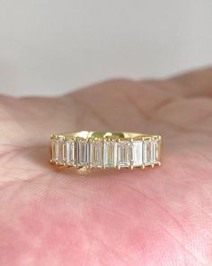 a woman's hand holding a gold ring with five baguettes