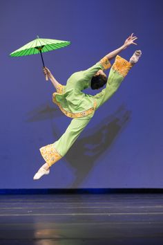 a person jumping in the air while holding an umbrella over their head and wearing a green outfit