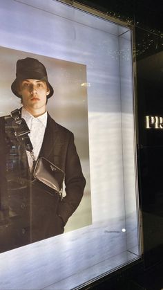 a man in a suit and hat standing next to a display case with an advertisement on it