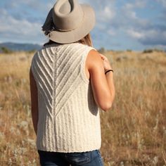 a woman standing in a field with a hat on her head looking at the sky