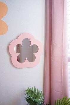 a pink flower shaped mirror mounted to the side of a wall next to a potted plant