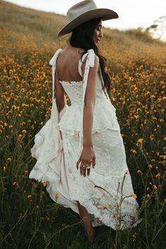 a woman in a white dress and hat walking through a field full of yellow flowers