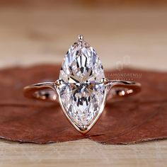 a pear shaped diamond ring sitting on top of a leaf