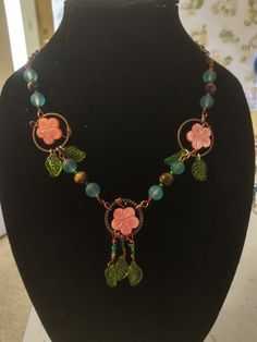 This beautiful necklace is part of the FantSea Stories collection. This necklace symbolizes the beautiful and lush gardens that flower throughout the islands. This necklace has carved pink flower beads, copper vines and swinging green leaves wrapped around delicate copper spheres. This necklace is graceful and delicate and full of beauty like the wearer of this necklace. Green Bohemian Copper Wire Necklace, Artisan Green Copper Necklace, Handmade Rose Gold Nature-inspired Necklaces, Unique Copper Flower Jewelry, Green Bohemian Flower Charm Necklace, Nature-inspired Green Flower Necklaces, Bohemian Necklace With Flower Charm And Round Beads, Bohemian Flower-shaped Wire Wrapped Jewelry, Bohemian Pink Wire Wrapped Necklace