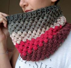 a woman wearing a white t - shirt is holding up a crocheted scarf