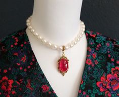 There is something about that gorgeous luster that makes us all love pearls.  This choker is elegant in its simplicity - just beautiful lustrous, creamy off-white oval pearls with a large ruby red stone and understated yet regal gold frame. The pearls are a good size - each one approximately 1/2 inch long and is the perfect size to stand with, but not be overpowered by, that bold red stone.  The stone is fused ruby ore and the pendant hangs 2 inches from the 14-1/2 inch choker.  It is sensationa Elegant Red Pearl Necklace, Elegant Red Pearl Necklace For Formal Occasions, Elegant Red Pearl Drop Necklace, Red Elegant Pearl Drop Necklace, Royal Ruby, Bridal Choker, White Freshwater Pearl, Pearl Choker, Choker Necklaces