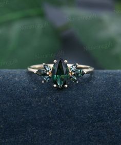 an emerald colored ring with three green stones on it's sides, sitting on top of a blue cloth