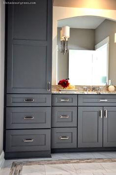 a bathroom with gray cabinets and marble counter tops, along with a large mirror on the wall