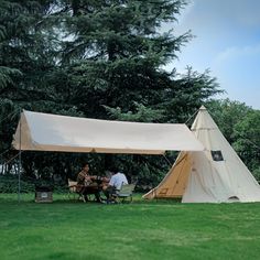 two people sitting at a picnic table in front of a teepee tent on the grass