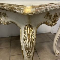 an ornate white and gold painted table on tile flooring with light shining through the top