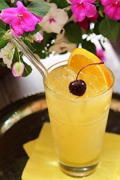 a drink with an orange slice and cherries on the rim next to pink flowers