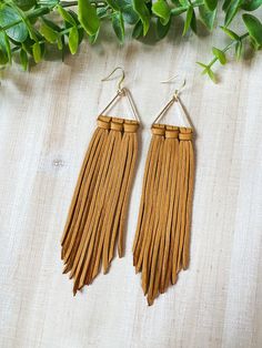 two pairs of brown leather tassels hanging from metal hooks on a white surface