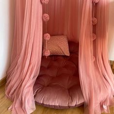 a pink canopy bed with pom poms hanging from it