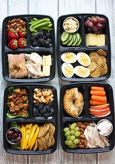 four black trays filled with different types of food on top of a wooden table