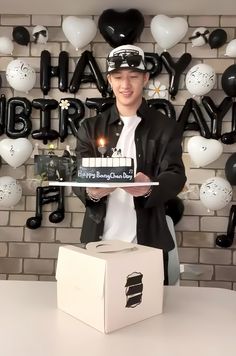 a man holding a birthday cake in front of a brick wall