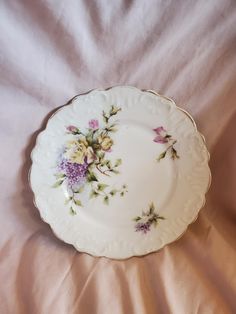 a white plate with flowers on it laying on a pink bed sheet in the sunlight