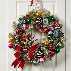 a christmas wreath hanging on a door with ornaments around it and a santa clause standing in the background