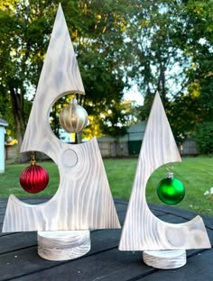 two metal christmas trees on top of a wooden table in front of some grass and trees