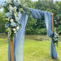 an outdoor wedding setup with blue drapes and flowers on the side, along with greenery