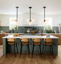 a kitchen island with four stools in front of it and three lights hanging from the ceiling