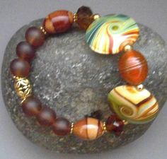 The beautiful 7-inch Southwestern-Boho-themed Mixed Stretch Bracelet of Porcelain Disks with vivid bands of Green and Dark Orange and Lampwork Glass beads is perfect for layering with other gold and gemstone bracelets.  An exquisite 16 X 12mm Handmade Orange with Gold-banded Lampwork Glass Bead is the central bead with Two large 25 X 20mm Polished Porcelain Disks with Green, Orange and Tan veins on either side.  Faceted 11 X 9 Czech Glass Rondel Beads in a Clear Sparkly Brown lead into 16 X 12mm Beads Christmas, Porcelain Beads, Southwestern Boho, Dark Orange, Evil Spirits, Lampwork Glass Beads, Gorgeous Bracelet, Boho Stil, Gemstone Bracelets