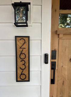 a wooden sign hanging on the side of a white house next to a black door