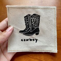 someone holding up a small patch with a cowboy boot on it's side and the word cowboy written in black