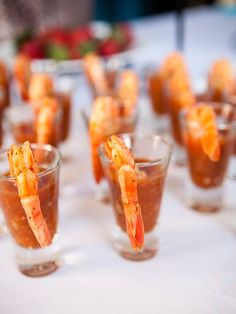 small glasses filled with shrimp and sauce on a white table cloth covered tablecloth, ready to be served