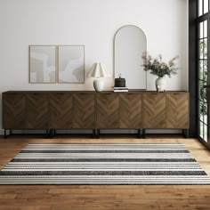 a room with a rug, mirror and two vases on the sideboard next to it