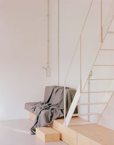 a bed sitting on top of a wooden step next to a stair case in a white room