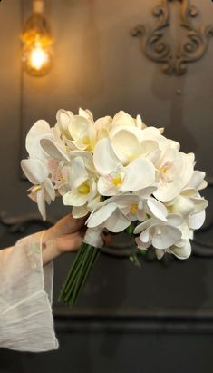 a woman holding a bouquet of white flowers in her hand with a light on the wall behind her