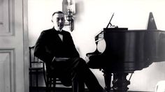 an old photo of a man sitting in front of a piano and looking at the camera