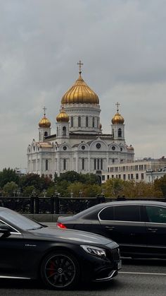 two cars parked in front of a large white building with gold domes on it's roof