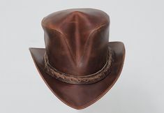 Hand Crafted Leather Premium Quality Leather Hat , Each Hat is Hand made  Description: we have multiple options in leather Color : Black , Dark Brown , Distress Brown , White , Silver , Maroon Redish  , Greenish Green ,  Tan Brown * High-Quality Craftsmanship handmade * Real Leather * 100% pure leather Sizing: XS 54 CM S 55-56 CM M 57-58 CM L 59 CM XL 60 CM XXL 61-62 CM Heads come in all sizes, and in a lots variety of shapes. Although high quality hats are adaptable, and will usually conform to differences in shape with a little wearing, it is essential that the size be correct for the head. To determine your hat size, measure the circumference around your head, keeping the tape level and firm, across the temples and above the eyebrow ridges. Check the size chart given below. For in-betwe Leather Top Hat, Steampunk Top, Brown Leather Top, Steampunk Top Hat, Clothing Tape, Victorian Hats, Steampunk Hat, Leather Hat, Top Hats