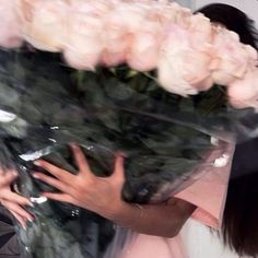 a woman holding a bouquet of flowers in front of her face with both hands on it