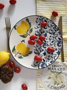 a plate with tomatoes and lemons on it next to a knife, fork and napkin