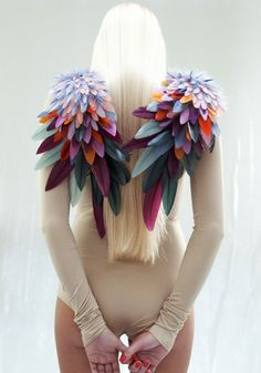 a woman with long blonde hair wearing gloves and feathers on her head is standing in front of a white background