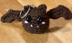 a brown stuffed animal keychain with black eyes and ears on top of a wooden floor