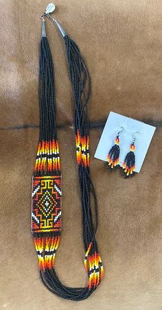 Authentic sterling silver Native made black beaded Aztec jewelry set. Featuring matching necklace and earrings. Aztec black, red, orange, & yellow strand necklace measures 28” inches length. Colorful fringed bottom handmade beaded earrings 2.5” inches length. Both of these beauties are Sterling silver. This set would make for a beautiful gift to a loved one or yourself. 😉 Cultural Jewelry, Aztec Bracelet, Aztec Jewelry, Western Fashion Jewelry, Beading Necklace, Native American Jewellery, Rodeo Jewelry, Necklaces Ideas, Native American Beadwork Patterns