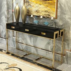 a black and gold console table with two vases on it in front of a painting