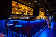 two bar stools sit in front of an illuminated bar