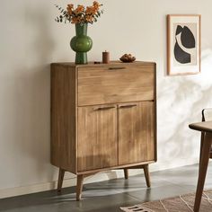 a wooden cabinet with two doors and drawers next to a table with flowers on it