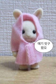 a small teddy bear wearing a pink outfit with a speech bubble in it's mouth