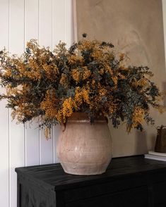 a vase filled with yellow flowers sitting on top of a black table next to a white wall