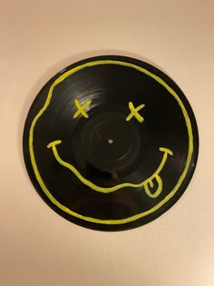 a black record with yellow smiley face drawn on it's side, hanging from the wall